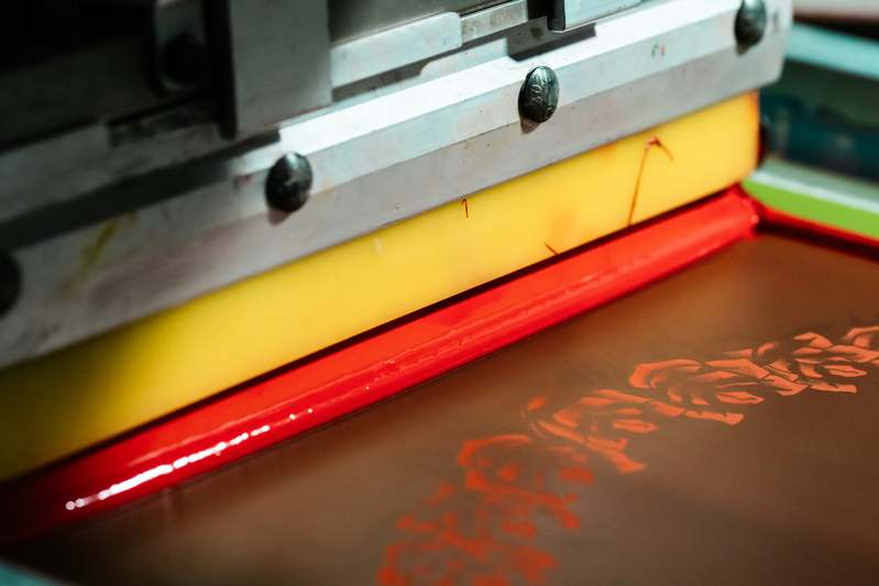 Two creators collaborating over a screen printing setup in a sunlit workshop